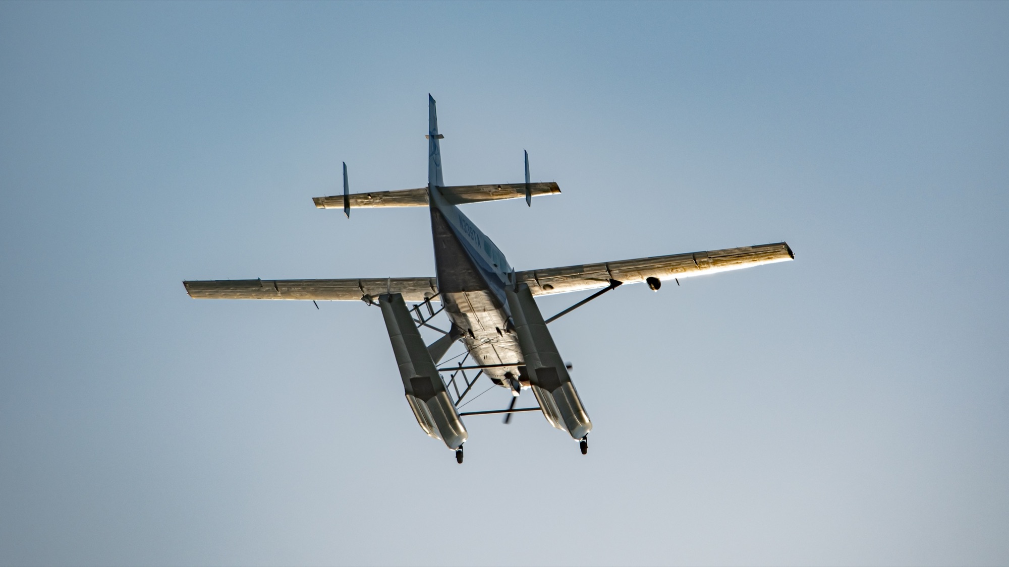 A Twin Otter on floats flying low against a clear sky.